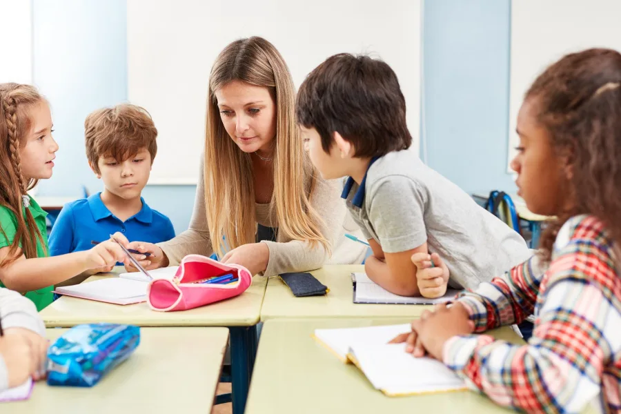 Lehrerin erklärt Kindern am Tisch eine Lernaufgabe