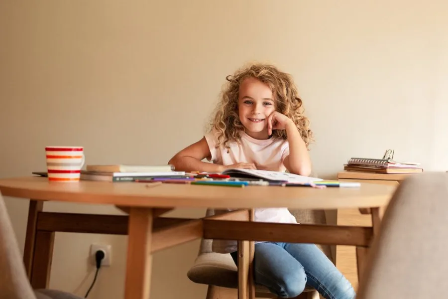 Mädchen sitzt lächelnd mit Schulbüchern am Tisch